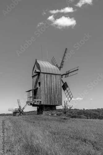 Old wodden windmill on a green meadow, field. Blue sky with white clouds. Old photo. Black and white photo.