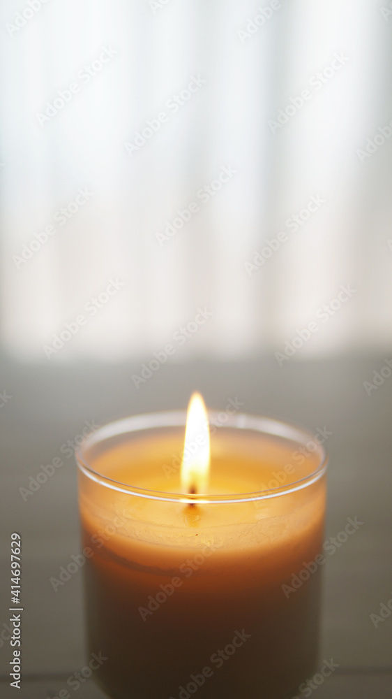close view of lit candle with a textured white and gray blurred background close view of lit candle with a textured white and gray blurred background