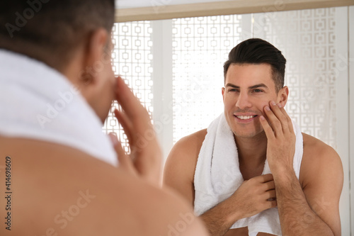 Handsome man with towel near mirror in bathroom