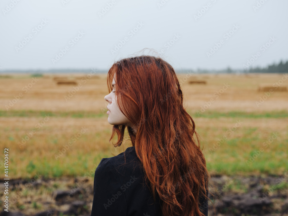 Portrait of a red-haired woman in a black dress in a field in nature cropped view Portrait of a red-haired woman in a black dress in a field in nature cropped view