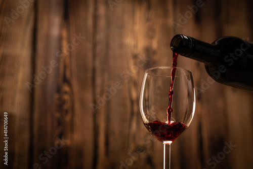 Pouring red wine into the glass against wooden blurred background.