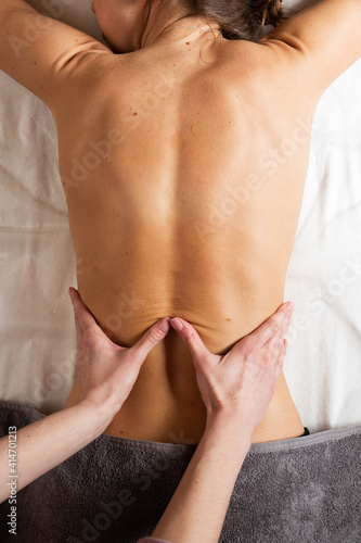 Relaxed young woman having healing body massage. Female therapist rubbing lady s back  giving her relaxing massage  top view  vertical orientation. Close-up masseuse hands doing back massage.