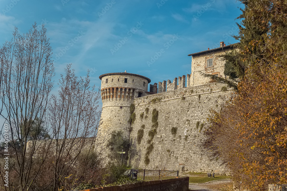 Part of the castle of the city of Brescia on a sunny winter day. A view on the tower and wall. Castello di Brescia, Lombardy, Italy. Medieval castle with battlements, a tower, drawbridge and ramparts.