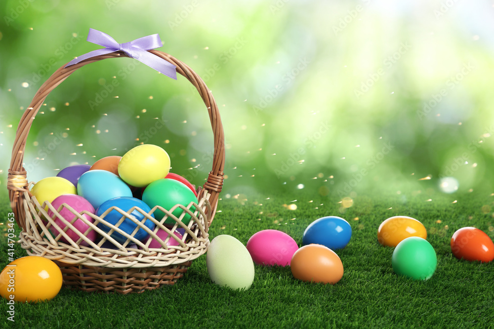 Wicker basket with bright painted Easter eggs on green grass outdoors