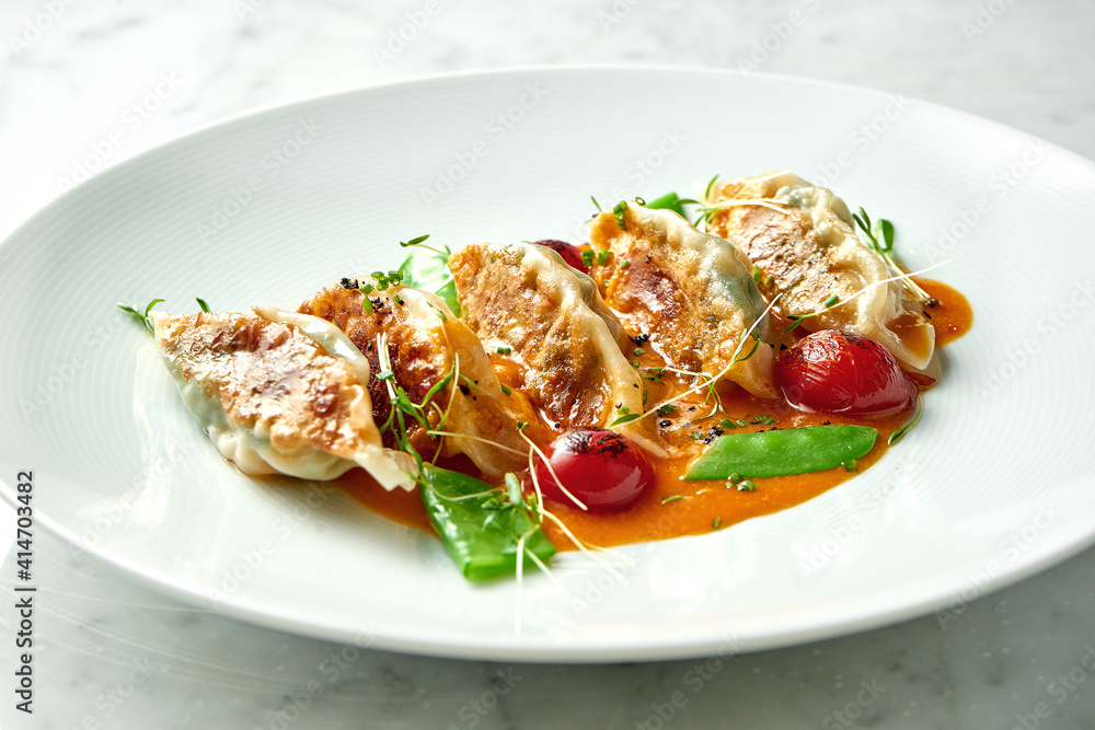 Fried dumplings or Japanese Gyoza in yellow sauce, cherry tomatoes and green peas, served in a white plate on a marble background. Pan-Asian cuisine. Restaurant food Fried dumplings or Japanese Gyoza in yellow sauce, cherry tomatoes and green peas, served in a white plate on a marble background. Pan-Asian cuisine. Restaurant food