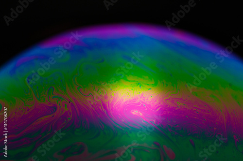 Rainbow soap bubble on a black background. Close-up of a colorful surface.