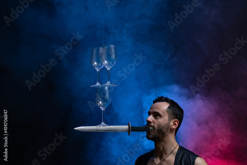 Man hold knife in the mouth and keep in balance wineglasses on it. concentration