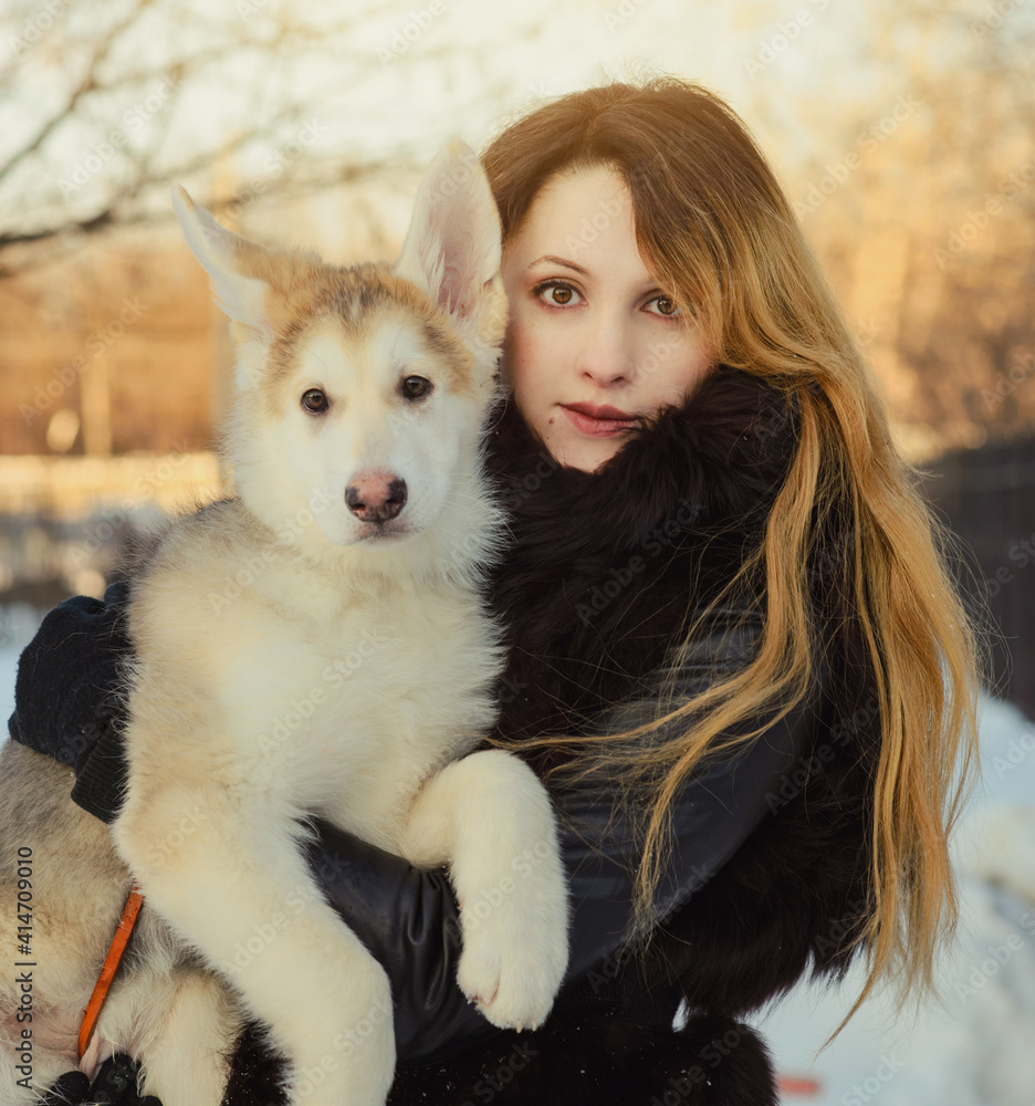 a young woman with long hair holds a puppy in her arms. a winter portrait
