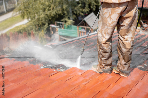 Man standing on rooftop and washing dirt from it. Before and after state of tiles.