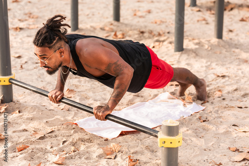 african american boy does push-up exercises on a barbell in a calisthenics park.