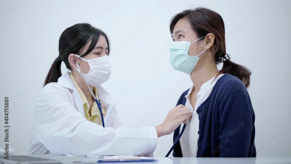 Young doctor wearing protective mask using stethoscope checking heartbeat of female patient.