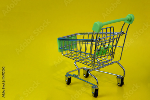 Shopping cart empty on yellow background, supermarket shopping concept. Place for an inscription. The concept of food prices in a supermarket, holiday discounts.