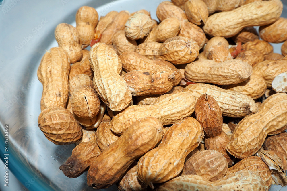 a lot of roasted peanuts in the shell lies in a glass bowl side view a lot of roasted peanuts in the shell lies in a glass bowl side view