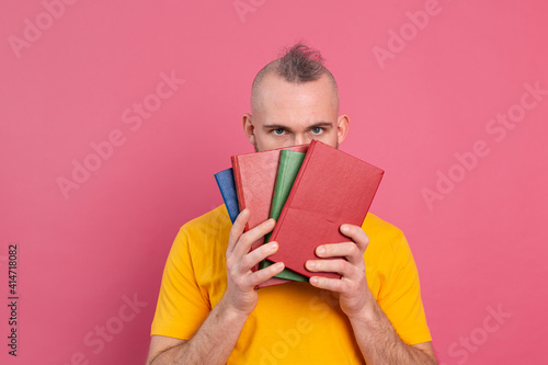 Adult smiling casual clothes guy with beard hugs favorite books to himself isolated on pink background