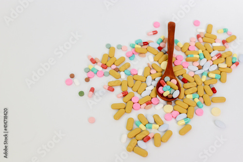 Various colorful multicolored pills on blue background. Tablets in a wooden spoon. Medicines, vitamins, antibiotics, and medicaments. Flat lay. First aid treatment and healthcare concept. Image with 