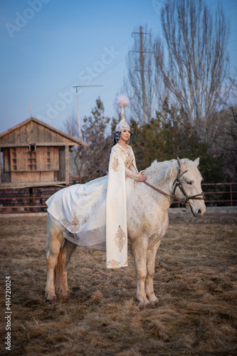 An Asian girl in a national costume is riding a horse. Kyrgyz national costume. © Urmat