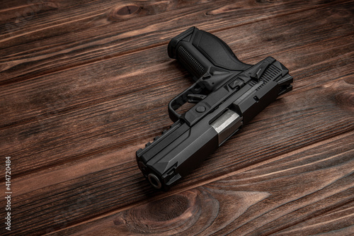 Black pistol on a brown wooden back. A short-barreled weapon for self-defense.