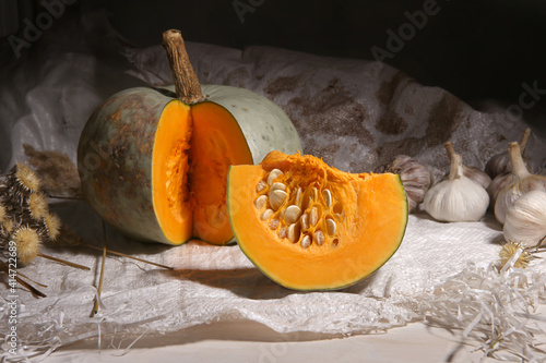 Still life of sliced pumpkin and garlics on plastic sack indoor. Ripe pumpkin and slice of pumpkin with seeds.