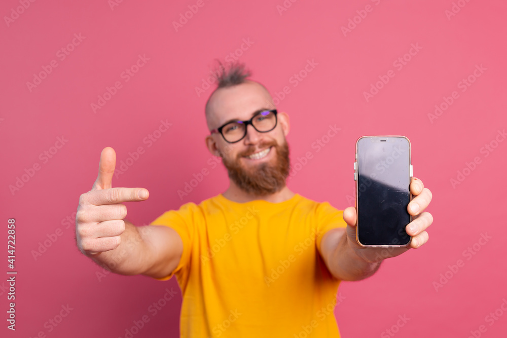 Hey something new. Happy european bearded guy pointing his cell phone with black blank screen, pink background isolated, free space Hey something new. Happy european bearded guy pointing his cell phone with black blank screen, pink background isolated, free space