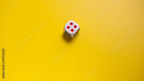 White dice with round dots number four on yellow background close-up. Concept of gambling and chance