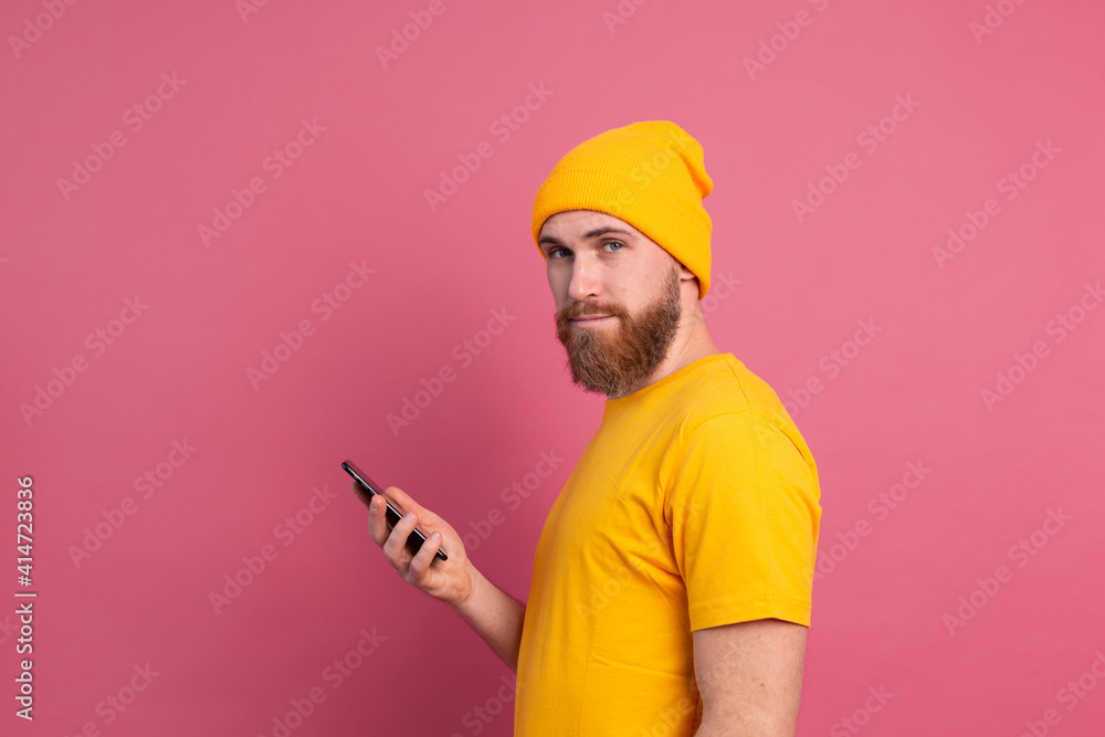 European handsome happy cheerful man with mobile phone smiling and look to camera pink background European handsome happy cheerful man with mobile phone smiling and look to camera pink background