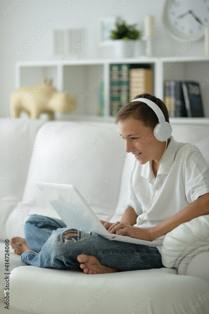 Cute boy in headphones in using laptop at home