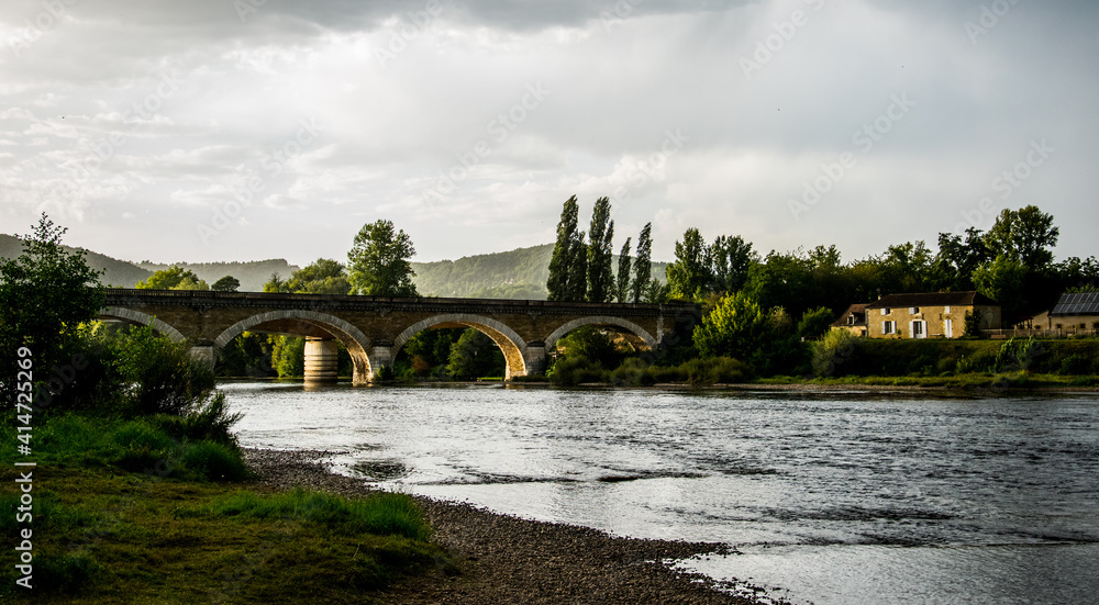 Puente sobre el río Dordoña y vegetación de ribera bajo las nubes de tormenta