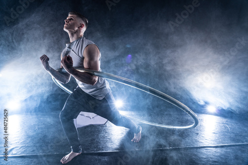 Cyr Wheel circus artist on smoked, dark background performing on stage 