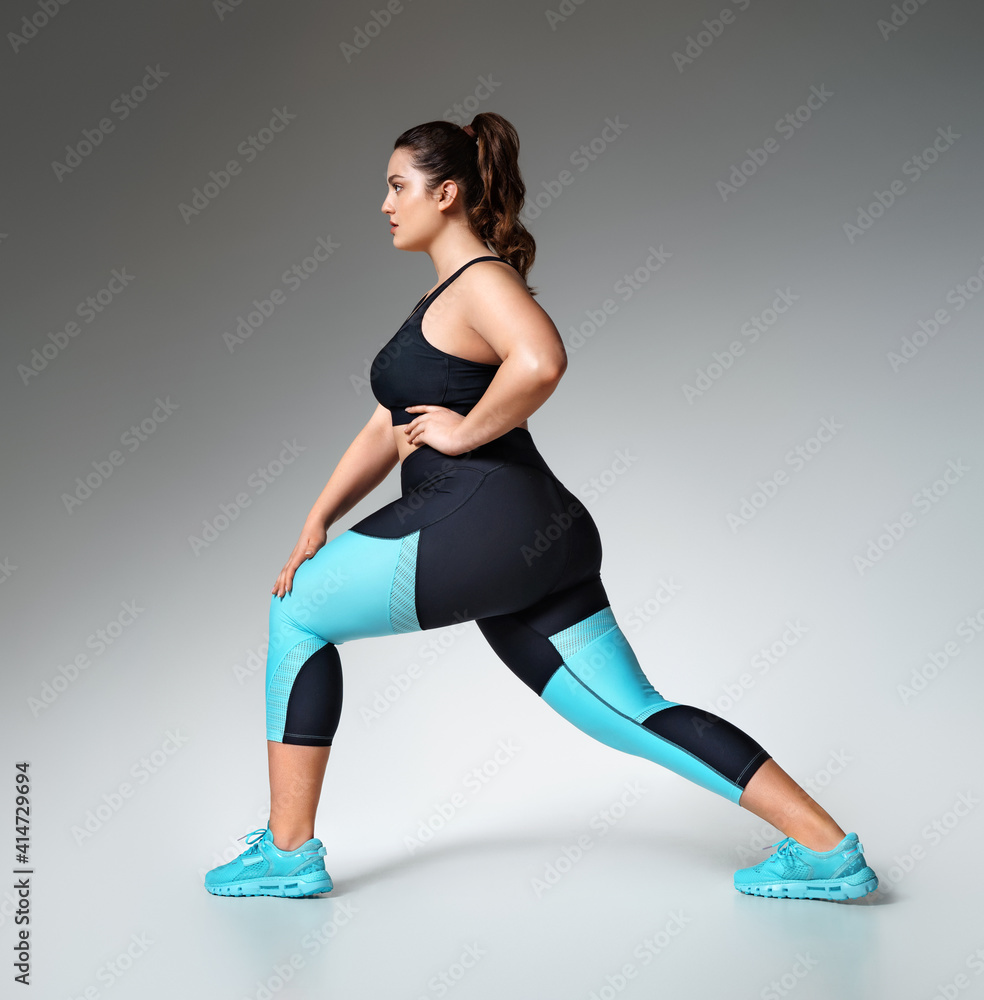 Warming up before training. Photo of model with curvy figure in fashionable sportswear on grey background. Sports motivation and healthy lifestyle Warming up before training. Photo of model with curvy figure in fashionable sportswear on grey background. Sports motivation and healthy lifestyle
