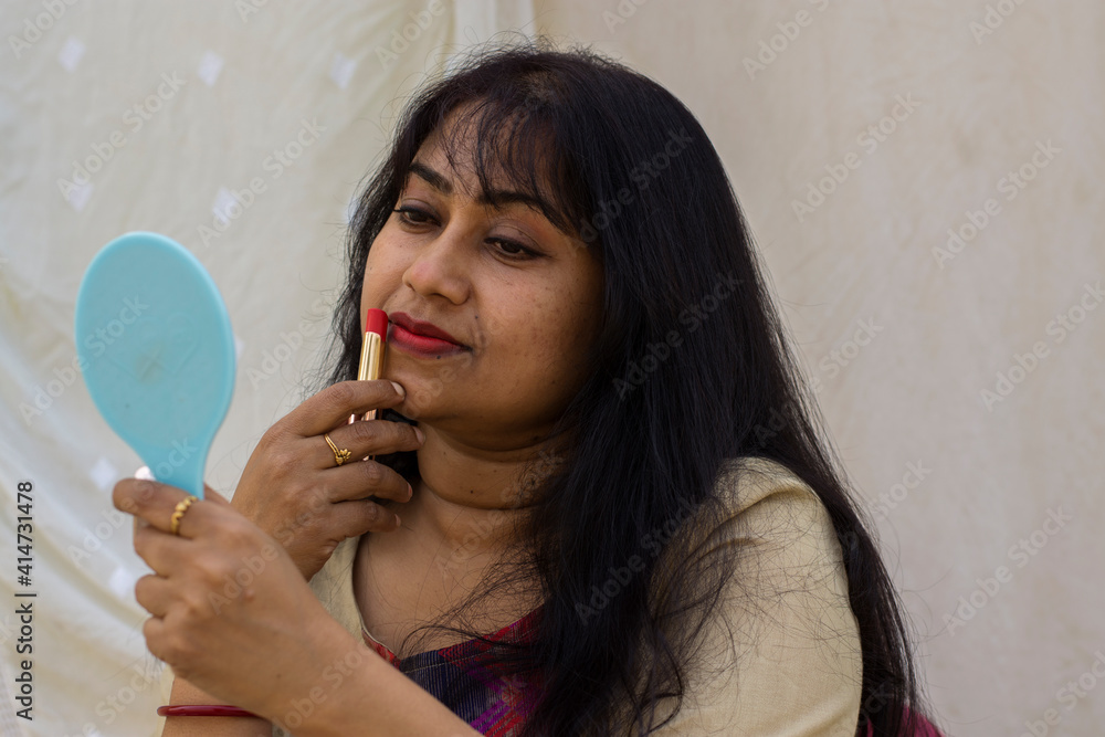 A beautiful Indian lady getting ready while applying lipstick and holding a mirror on her hand. A beautiful Indian lady getting ready while applying lipstick and holding a mirror on her hand.