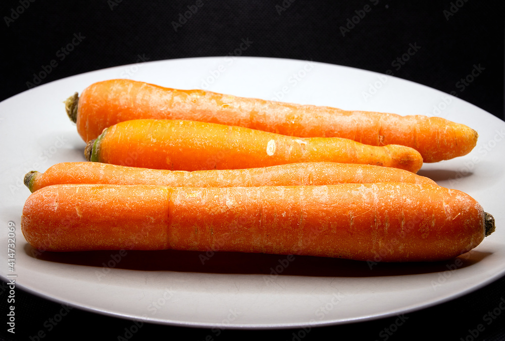 Four raw organic carrots on a white porcelain plate closeup Four raw organic carrots on a white porcelain plate closeup