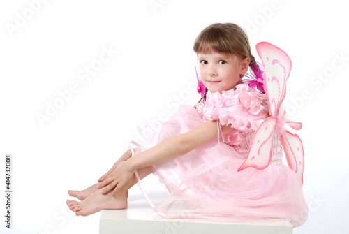 a beautiful little girl in a pink dress with butterfly wings is sitting on a table on a white background.