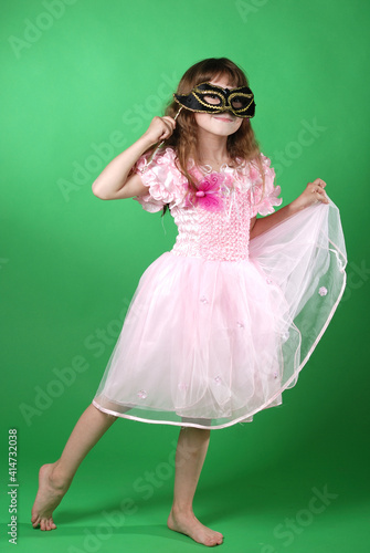 beautiful little girl in pink butterfly dress and carnival mask dancing on green background