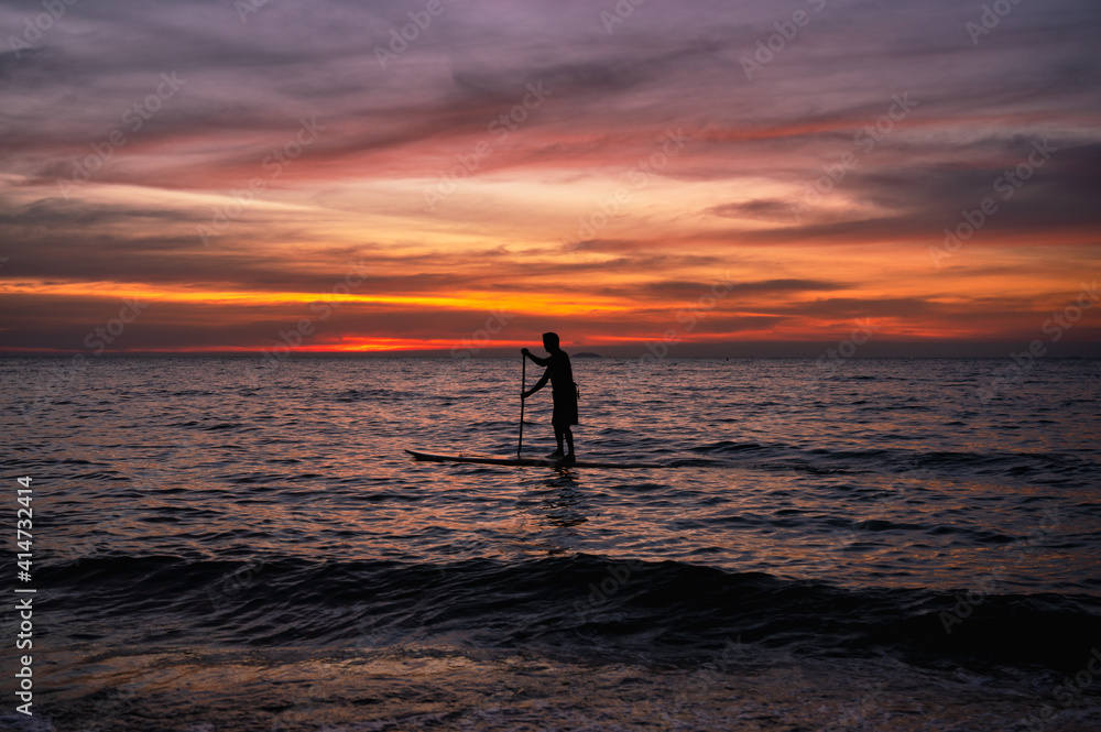 Silhouette man paddling sub board on the sea and colorful sky