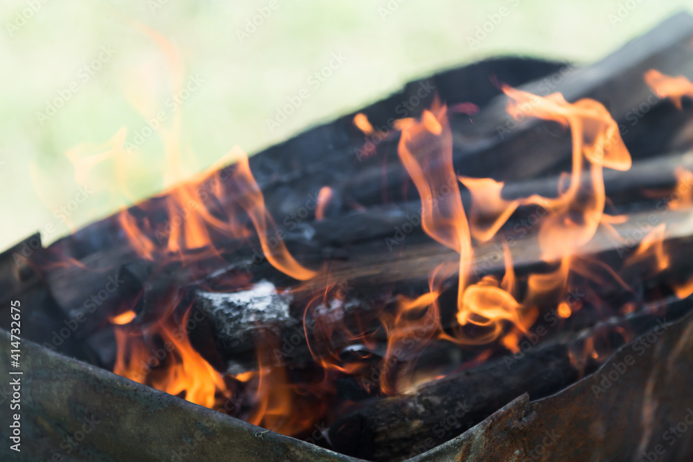 defocused orange flame of a campfire for barbecue in summer on green grass background