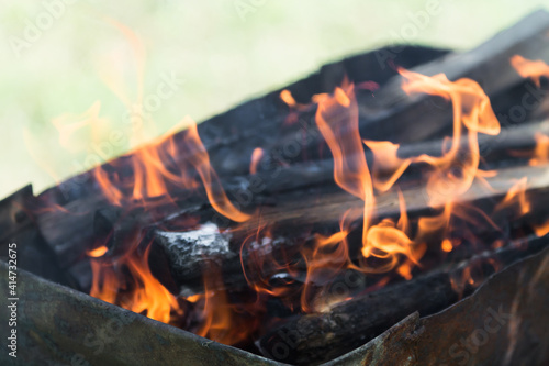 defocused orange flame of a campfire for barbecue in summer on green grass background