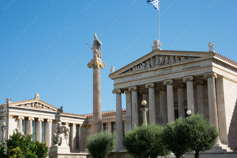 Academy of Athens neoclassical building with statues, flag and blue sky