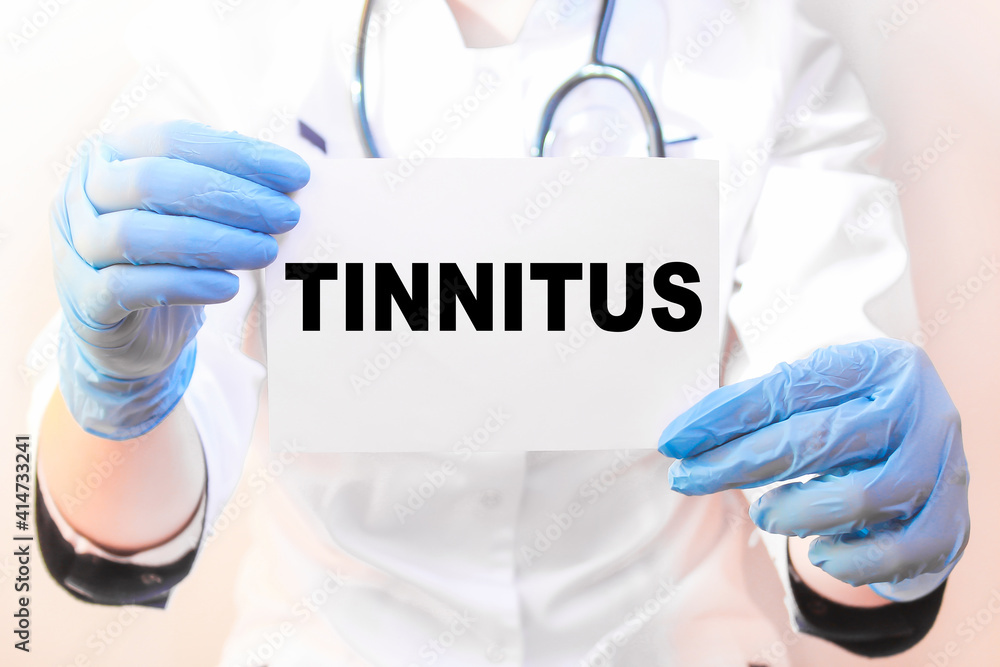 The doctor's blue - gloved hands show the word TINNITUS - . a gloved hand on a white background. Medical concept. the medicine The doctor's blue - gloved hands show the word TINNITUS - . a gloved hand on a white background. Medical concept. the medicine