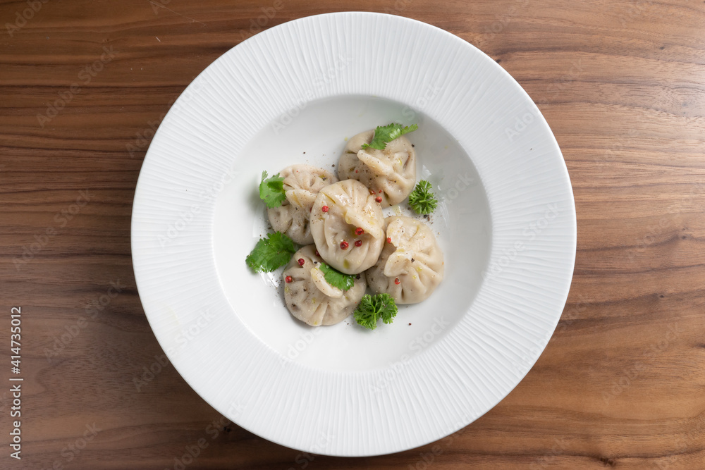 Boiled traditional asian dumplings manti sprinkled with parsley and red pepper in a white plate on a wooden table