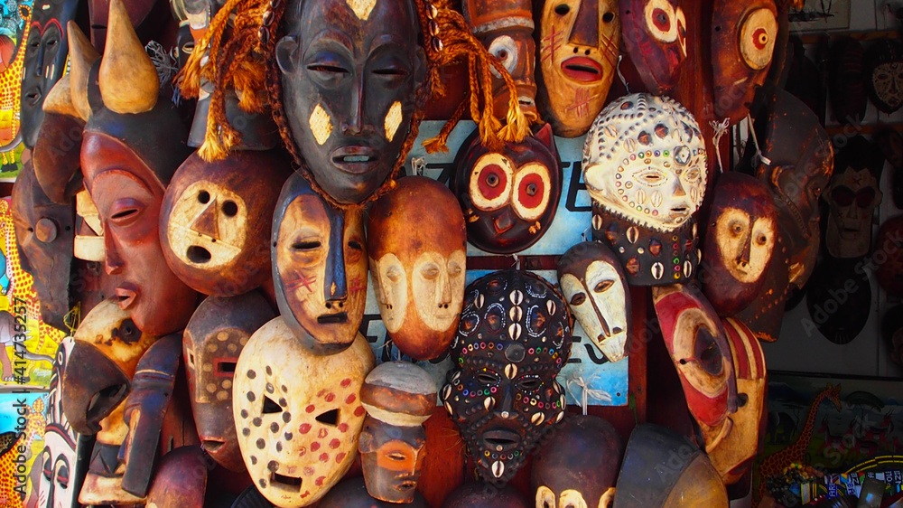 Selection of African masks carved from wood and decorated, some with seashells and others by being engraved - obrazy, fototapety, plakaty 