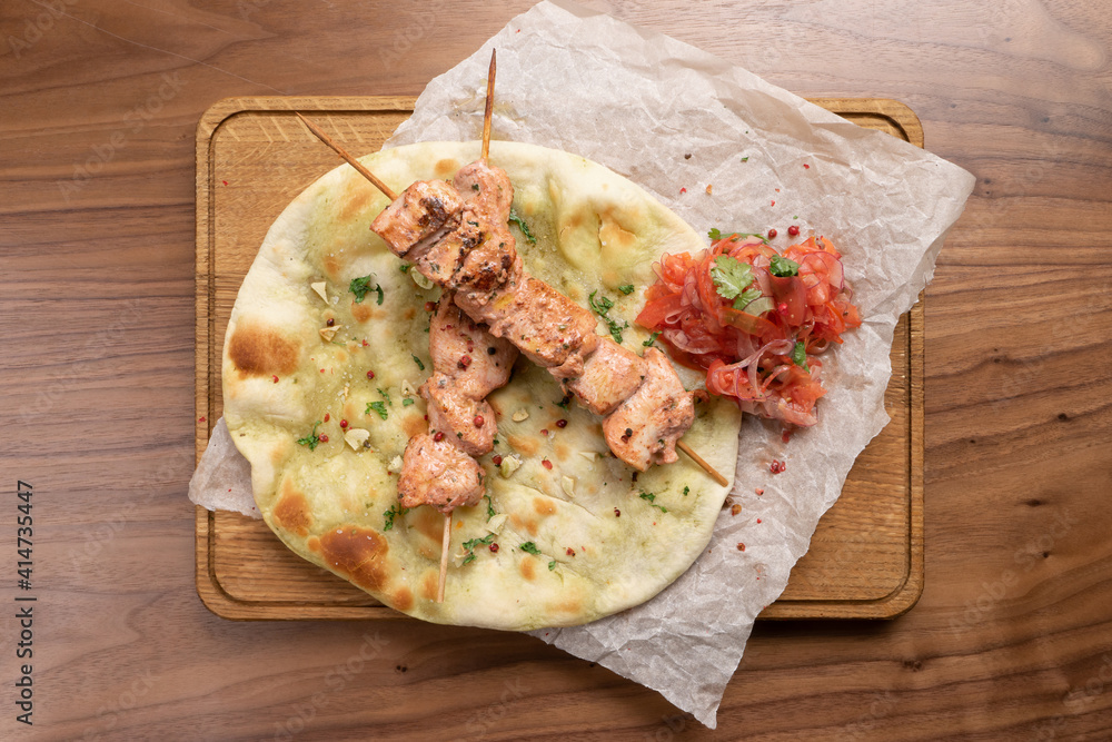 Hot pork kebab with tomatoes, onions and freshly baked tortilla on a wooden cutting board. Traditional Eastern dish of meat roasted on the grill. Hot pork kebab with tomatoes, onions and freshly baked tortilla on a wooden cutting board. Traditional Eastern dish of meat roasted on the grill.