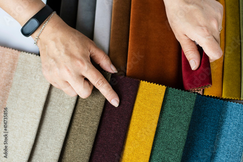 A woman in a store chooses a fabric for upholstered furniture in her new apartment, points to the color she liked in the catalog of special fabrics, close up