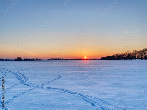 Backlit photo of a snowbounded plain in the light of the setting sun.