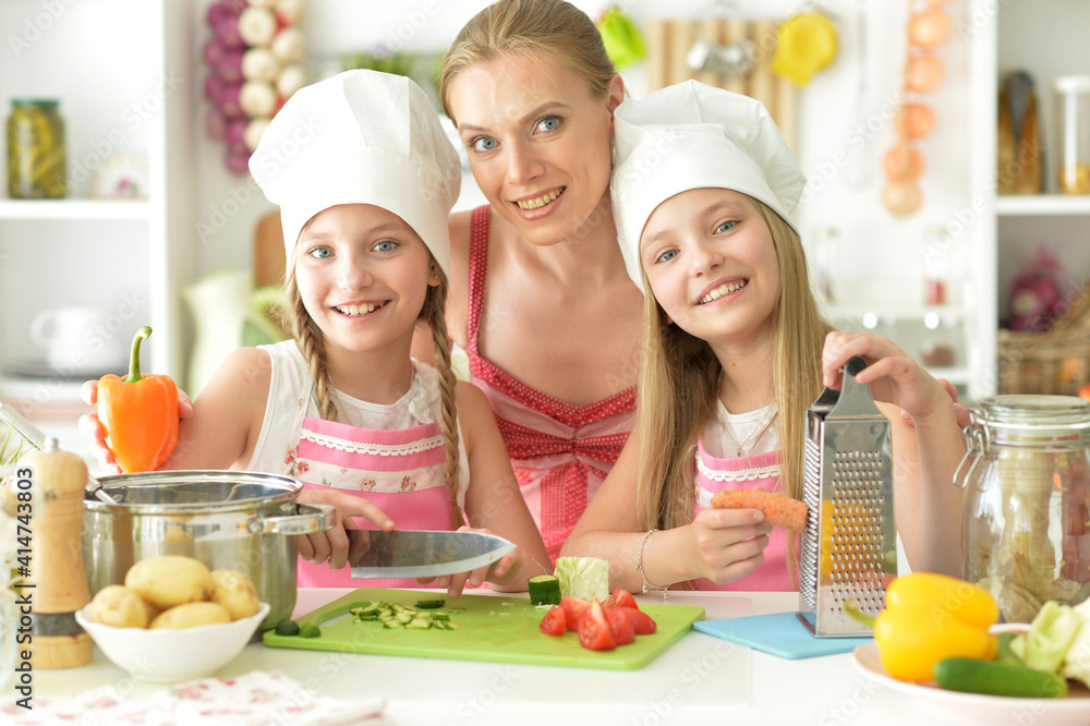 Cute girls with mother preparing delicious fresh salad in kitchen