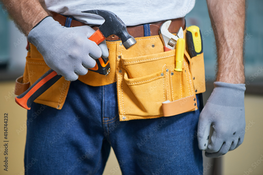 Ready to fix anything. Close up of repairman wearing a tool belt with various tools, holding a hammer in his hand Ready to fix anything. Close up of repairman wearing a tool belt with various tools, holding a hammer in his hand