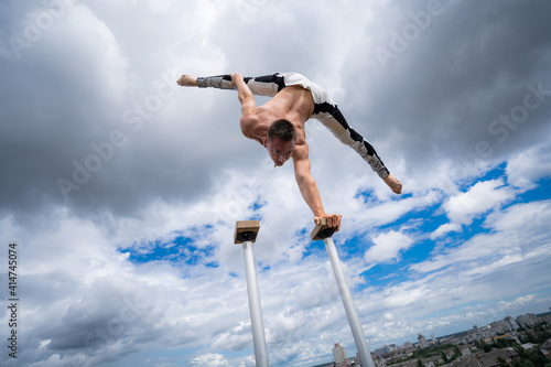 Flexible male circus Artist keep balance by one hand against amazing cloudscape. Individuality, outstanding and originality.