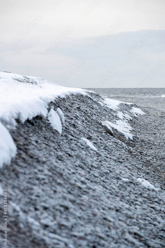 Snow covered cobblestone beach with ocean background