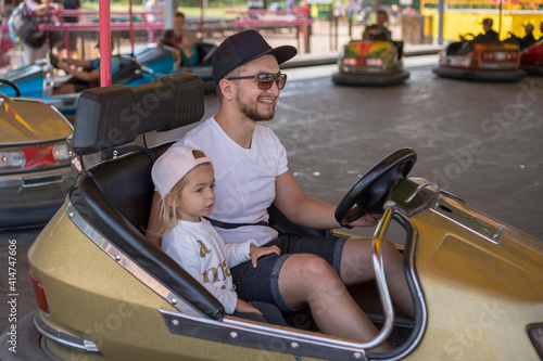 Father and daughter in bumper car at fun fair.