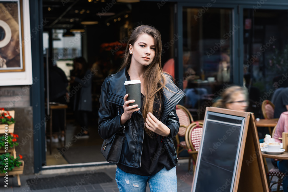 Pleasant young female with hot takeaway beverage leaving cafe Pleasant young female with hot takeaway beverage leaving cafe