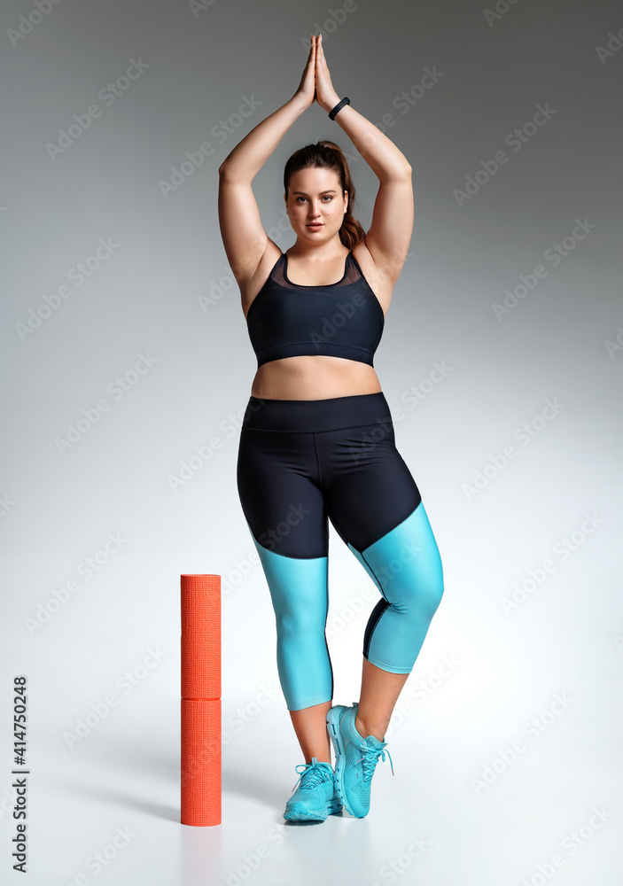 Young girl ready to yoga. Photo of model with curvy figure in fashionable sportswear on grey background. Sports motivation and healthy lifestyle Young girl ready to yoga. Photo of model with curvy figure in fashionable sportswear on grey background. Sports motivation and healthy lifestyle
